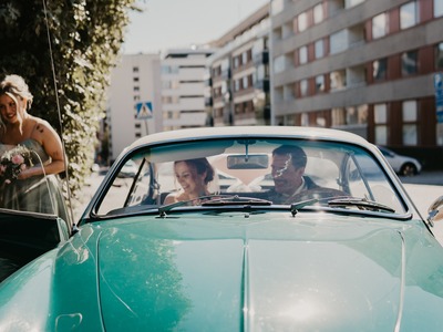 Hääpari nauraa hääautossa.